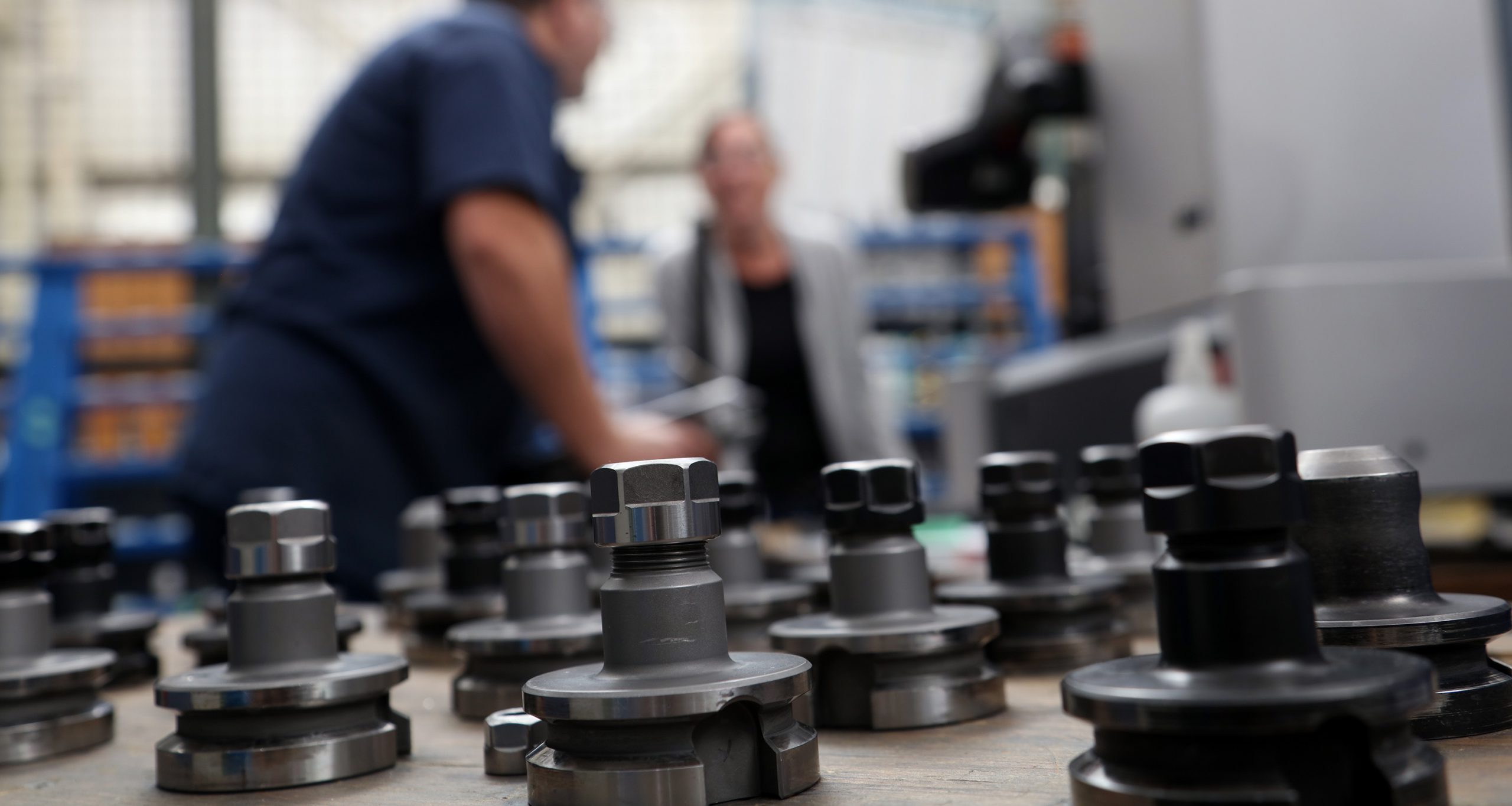 close up of metal components with two employees, talking, in the background