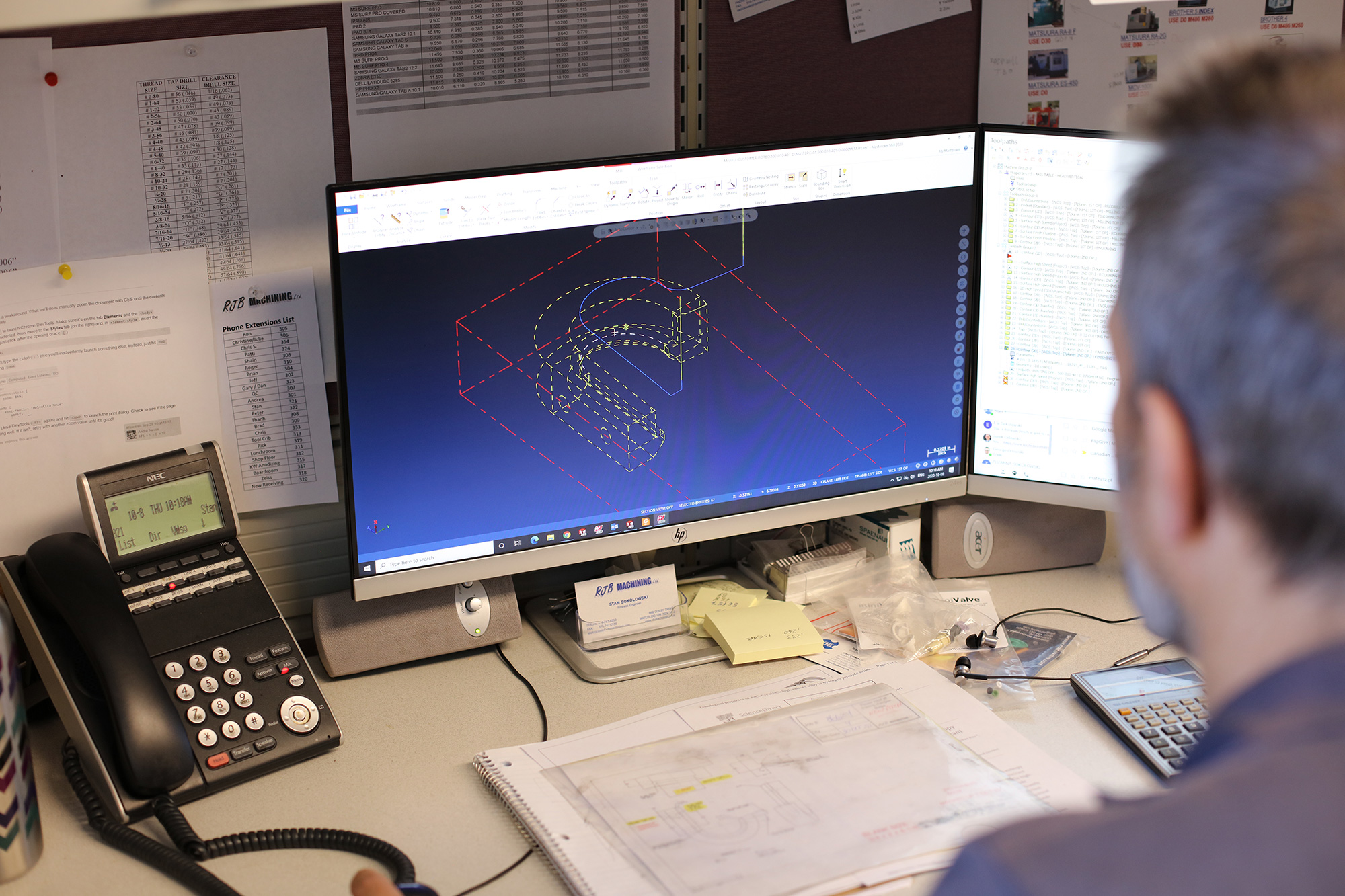 an employee sits at a desktop computer that displays a design rendering of a component