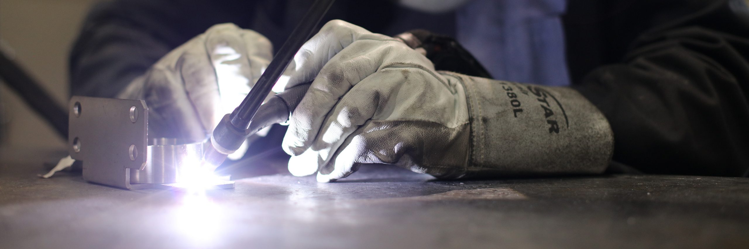 two gloved hands use a welding gun on a component