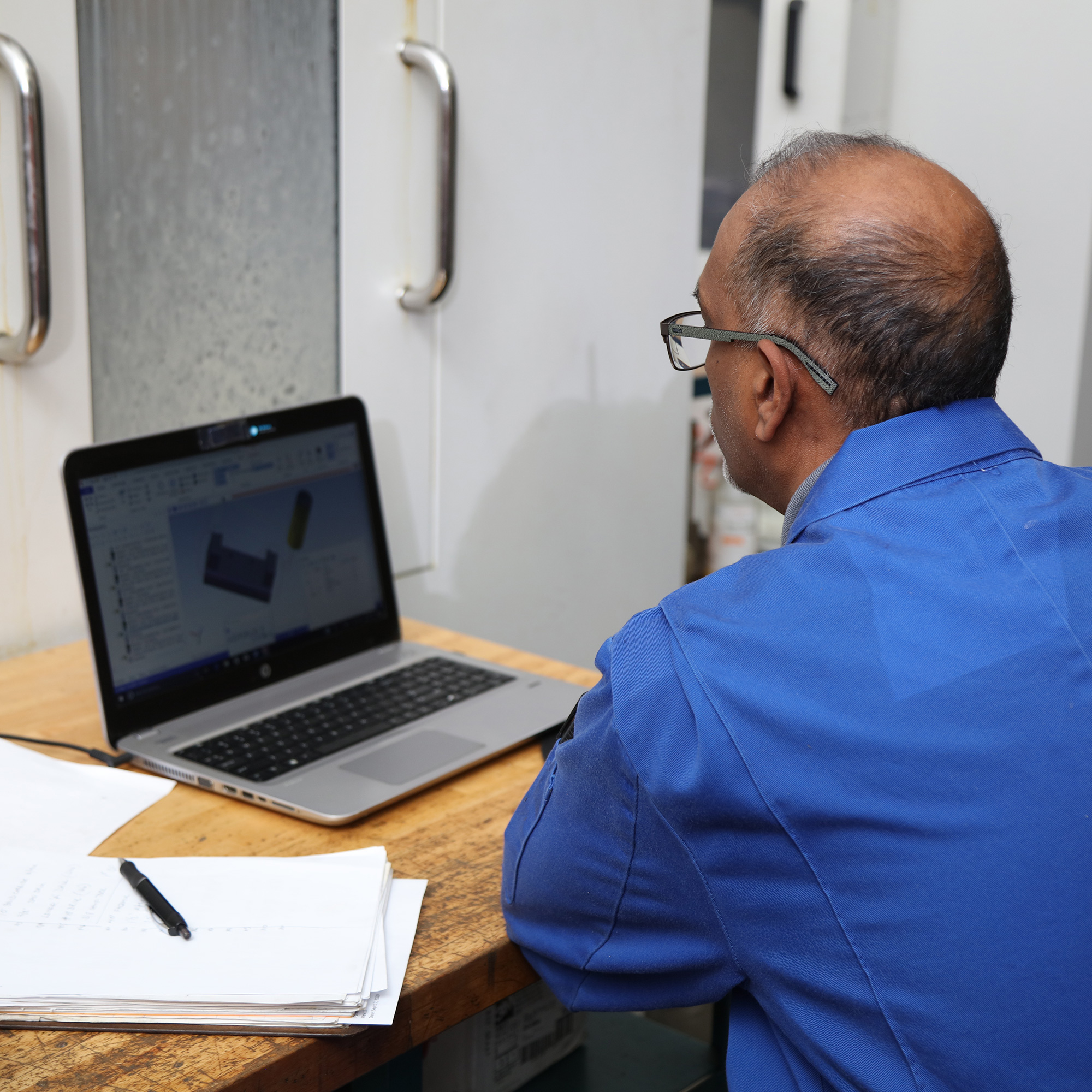 an employee sits at a desk looking at a laptop with a notebook beside it