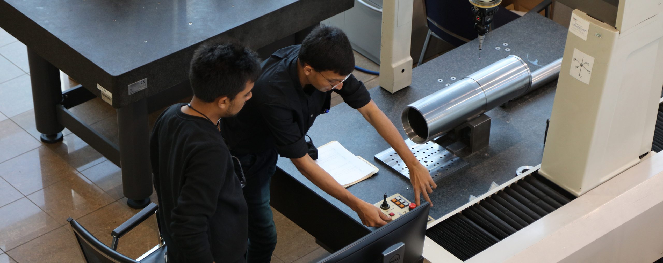 two emplyees standing over a machine looking down at the controls