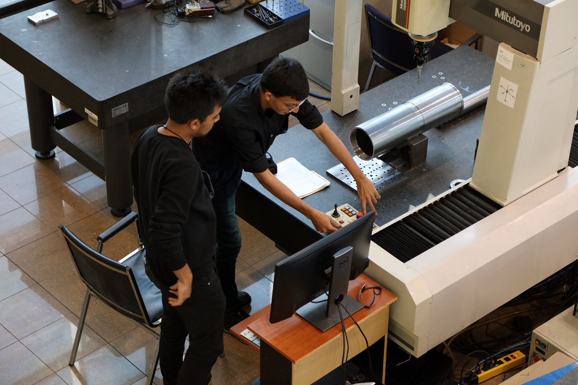 two employees look down at the controls of a machine