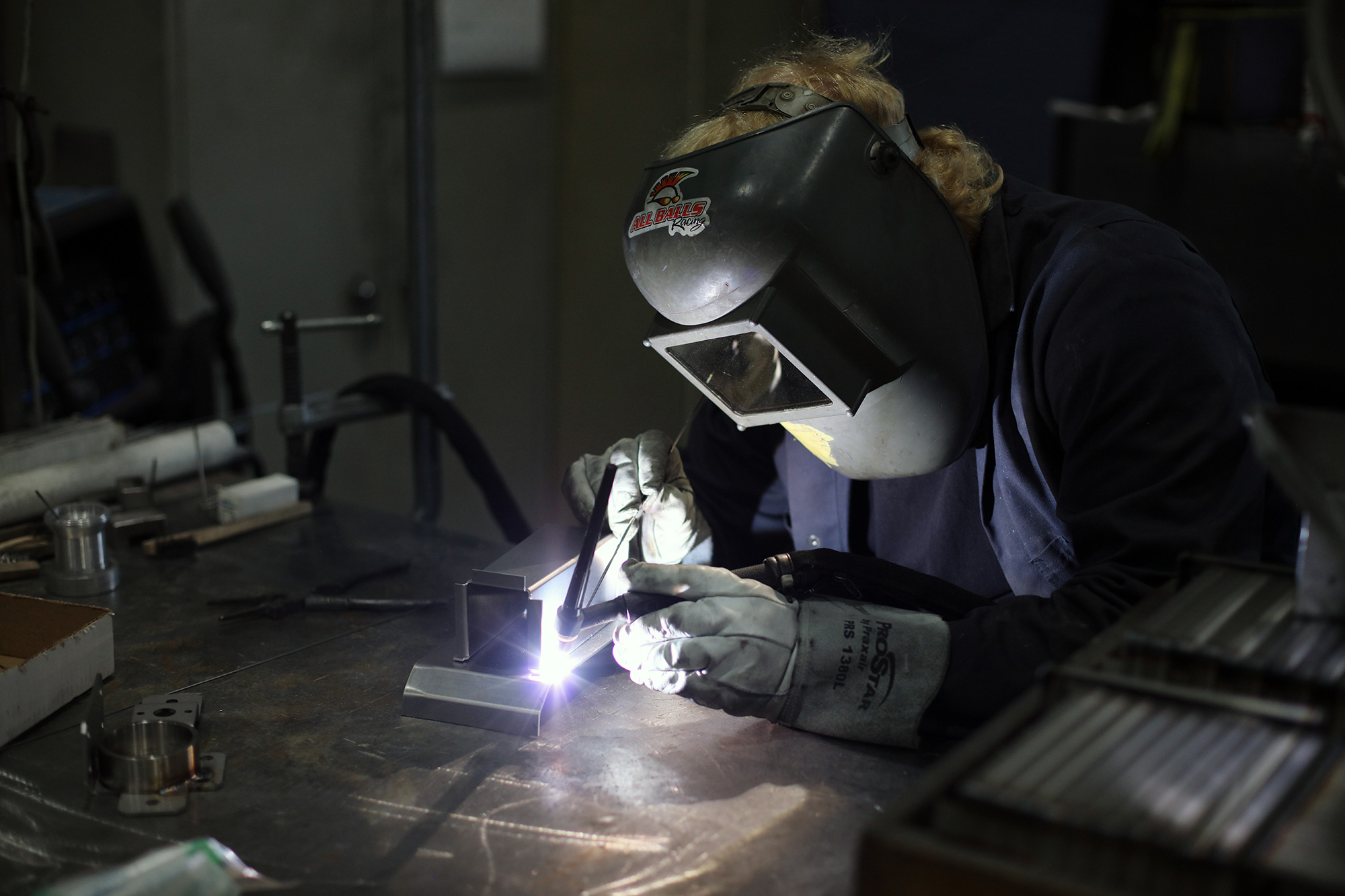 an employee welds a component wearing a welding mask and protective gloves