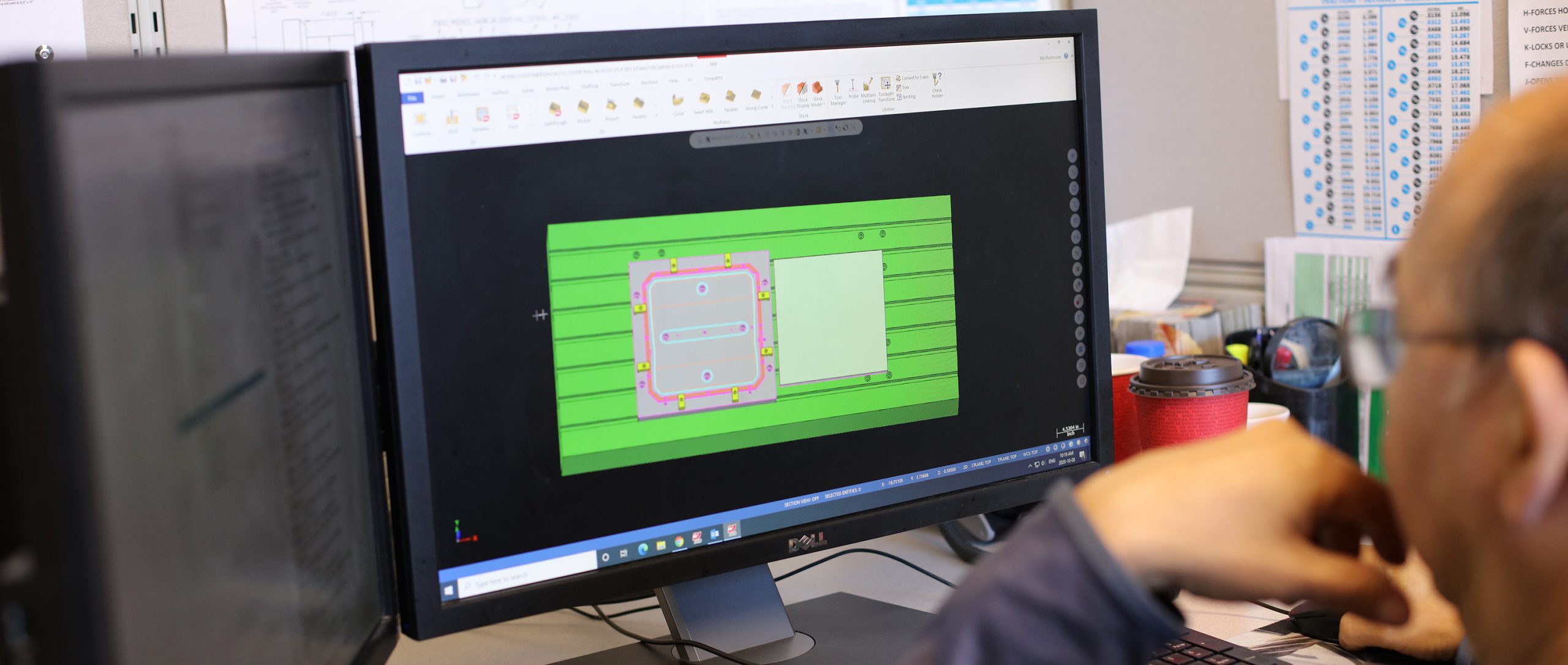 an employee sits at a desk looking at a computer that displays a design rendering of a component