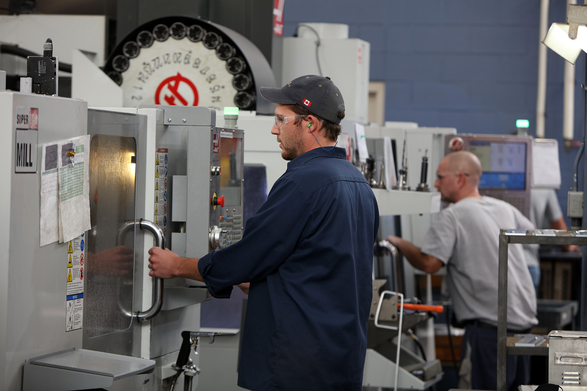 an employee holding onto the handle of a machining centre with another employee operating a different machine in the background