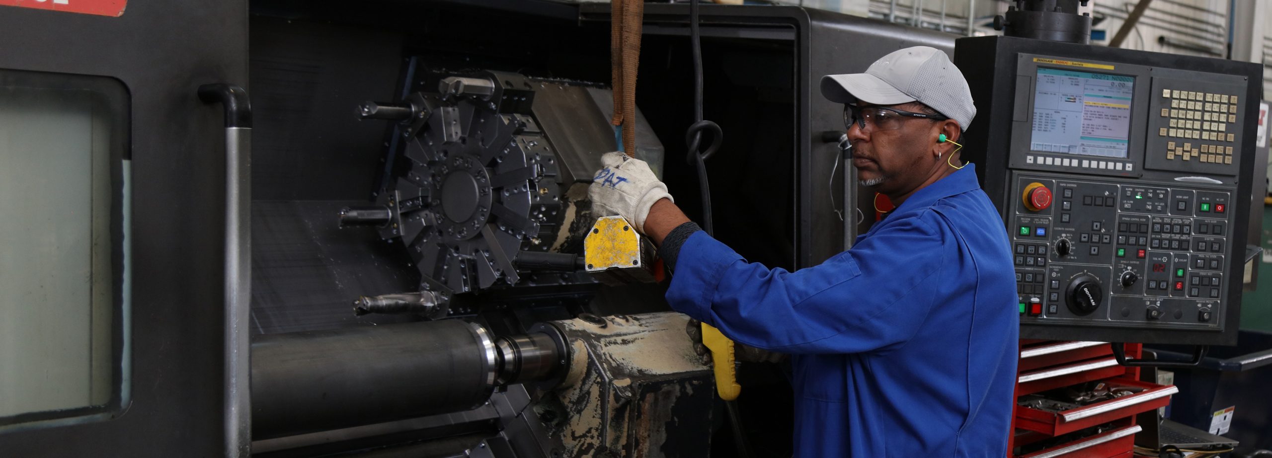 an employee wearing safety glasses and earplugs stands at the operating controls of a machining centre