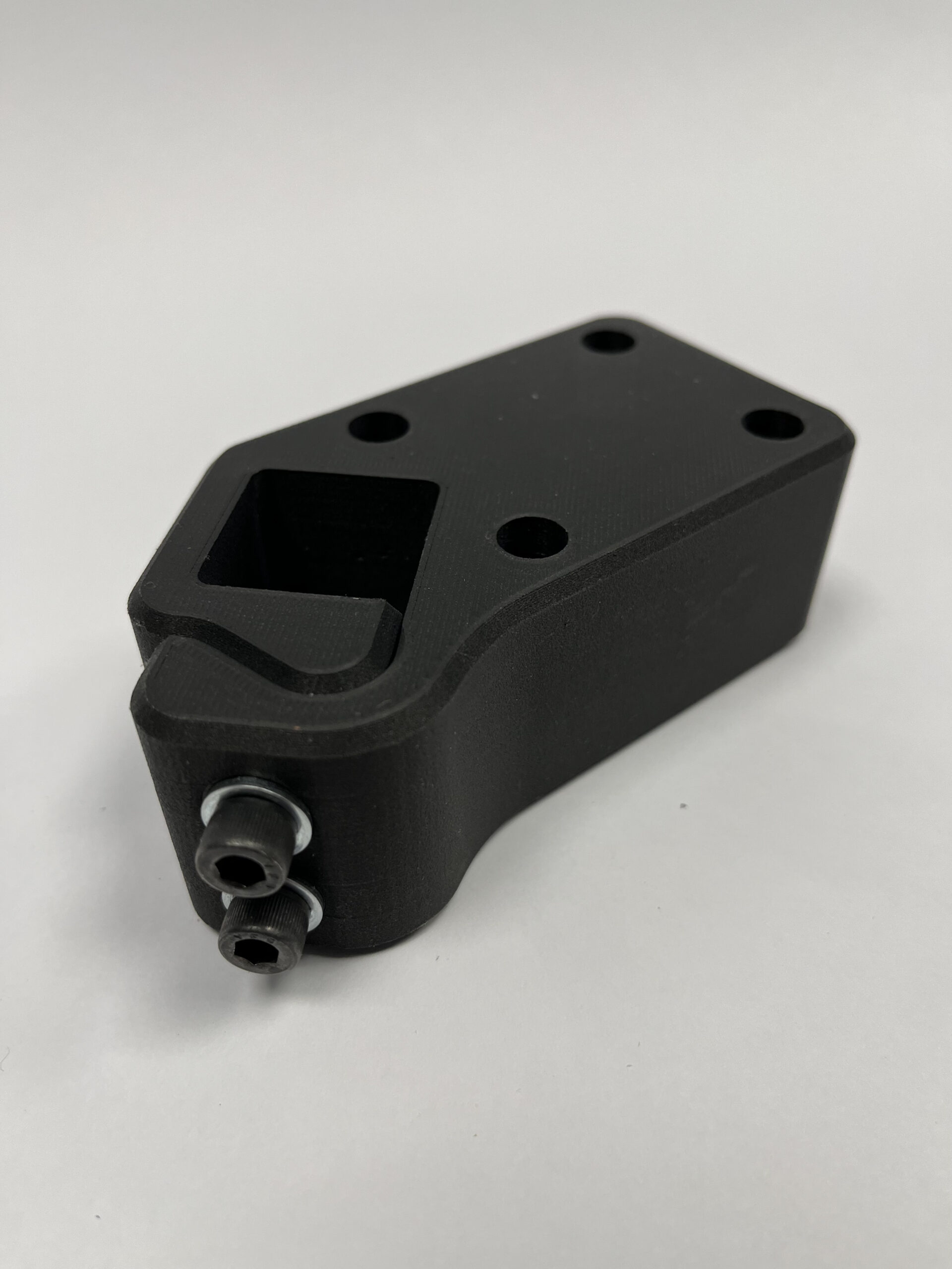 a 3D printed square black composite with 4 circles on top and to knobs on the side.