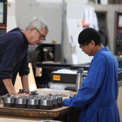 two employees stand at a table looking at components